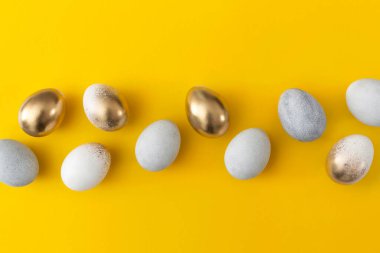 Sarı arka planda altın ve gri yumurtalar. Asgari paskalya kavramı.