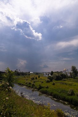 White clouds over the small river and ancient white buildings of monastery, Russia, Suzdal, landscape