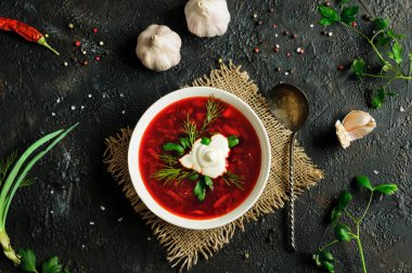 Bir kap kırmızı çorbanın en üst görüntüsü. Baharat ve otlarla kaplı koyu bir arka planda Ukrayna borşu. Gün ışığı ışığı. Seçici odak
