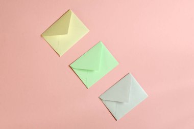 Pembe arka planda üç farklı renk zarfının minimalist kompozisyonu. Düz yatıyordu. Kopyalama alanı olan üst görünüm