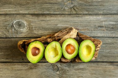 Avokado bir tahta parçası üzerinde ve tahta bir masanın üzerinde yarımlar. Kopyalama alanı olan üst görünüm
