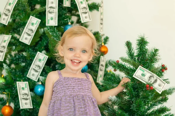 Little girl posing near the christmas tree decorated with dollar — Stock Photo, Image