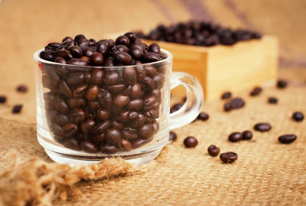 Cup with roasted coffee beans on the burlap background — Stock Photo, Image