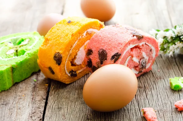 Bright rolled cake of different color on wooden table — Stock Photo, Image