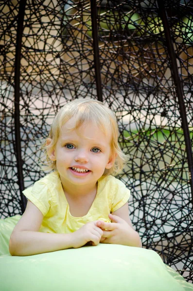 Little girl smiles  sitting in a wicker chair — Stock Photo, Image