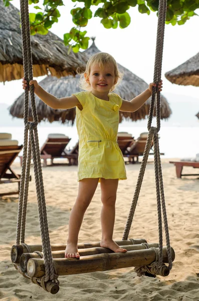 Little girl swinging with the beach in the background — Stock Photo, Image