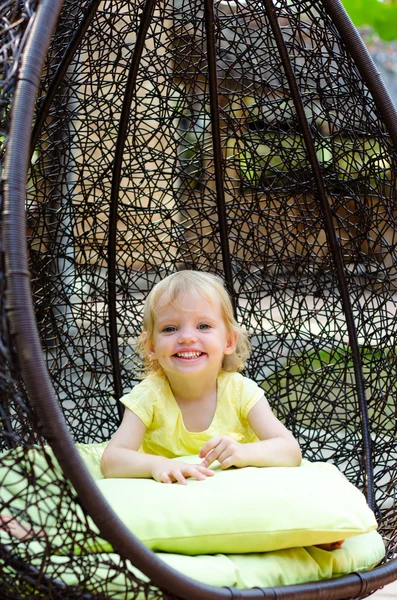 Little girl smiles  sitting in a wicker chair — Stock Photo, Image