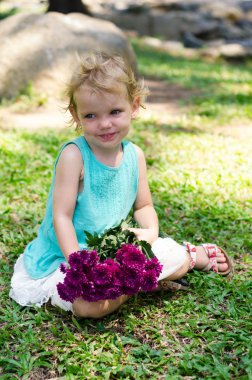 little girl with purple flowers bouquet on green grass