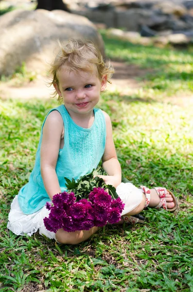 Little girl with purple flowers bouquet on green grass — Stock Photo, Image