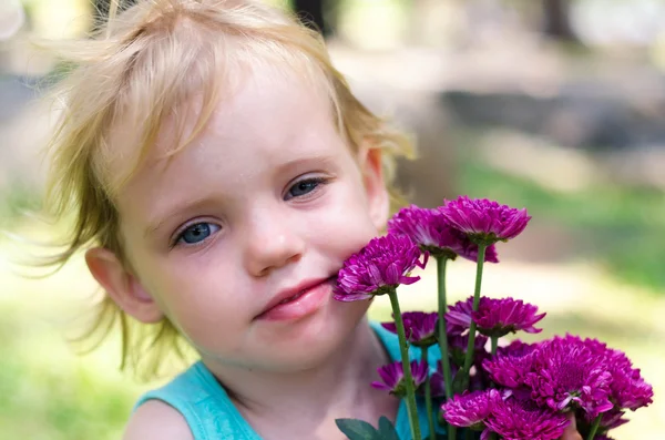 Little girl with purple flowers bouquet on green grass — Stock fotografie