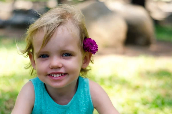 Little girl with purple flower on her head on green grass — Stock fotografie