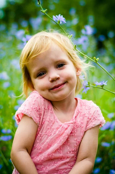 Cute little girl sitting in front of blue flowers field — Stock Photo, Image