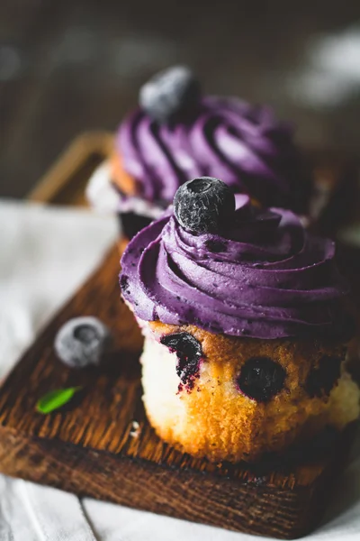 Blueberry muffins med lila smörkräm på träplatta, närbild. Selektiv inriktning, tonas bild — Stockfoto