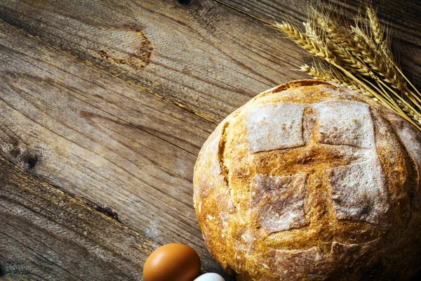 Selský chléb, pšenice golden uši a čerstvá vejce na dřevěné pozadí — Stock fotografie