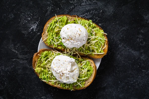 Tostadas de aguacate y huevo escalfado sobre fondo negro texturizado, vista superior — Foto de Stock