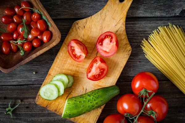 Fresh cooking ingredients on wooden cutting board. Tomatoes and cucumbers