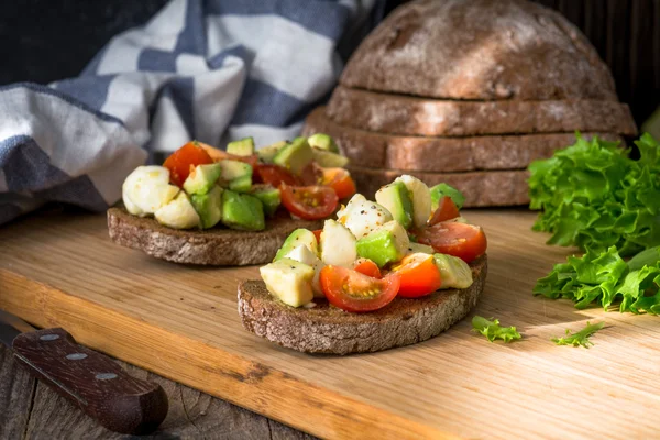 Gezond voorgerecht bruschetta met avocado, tomaat en mozzarella — Stockfoto