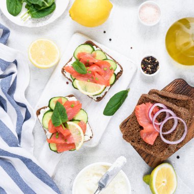 Krem peynirli somon sandviçi, beyaz ahşap tahtada servis edilen salatalık, üst manzara. Düz konum, kare ekin