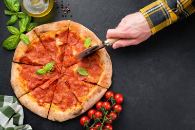 Siyah beton arka planda Pepperoni pizza. Erkek eli pizza bıçağıyla pizza dilimliyor. Üst görünüm kopyalama alanı
