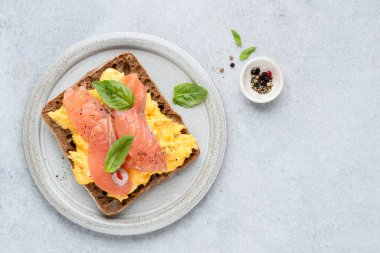 Çavdar ekmeğine çırpılmış yumurta ve füme somon. Üst Manzara. Sağlıklı kahvaltı ya da öğle yemeği sandviçi. Gri beton arkaplan, kopyala