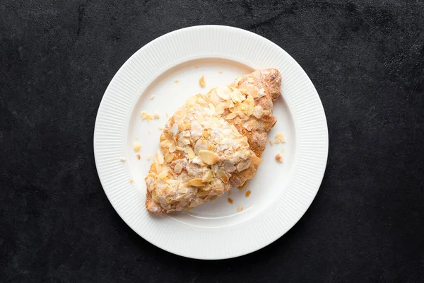 Beyaz tabakta tatlı badem kruvasanı, siyah beton arka plan, üst manzara. Fransız pastası.