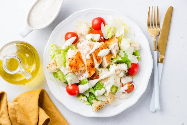 Caesar salad with grilled chicken and cherry tomatoes on white plate garnished with famous caesar sauce, top view. Healthy popular vegetable salad with chicken