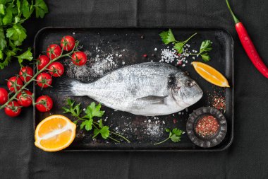 Çiğ Dorado balığı, baharatlar ve sebzeler eski siyah metal yemek tepsisinde pişirmek için.