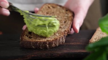 Çavdar ekmekli tostun üstüne avokado püresi serpiştirmek, yakın çekim. Sağlıklı vejetaryen atıştırmalığı, öğle yemeği ya da kahvaltılık avokado tostu