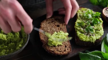 Çavdar ekmeğine püre avokado dök. Erkek el, avokado, tohum ve kişniş ile sağlıklı vegan tostu hazırla.