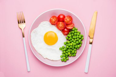 Yeşil bezelyeli sahanda yumurta ve pembe tabakta domates. Pembe arka planda izole edilmiş. Sağlıklı kahvaltı.