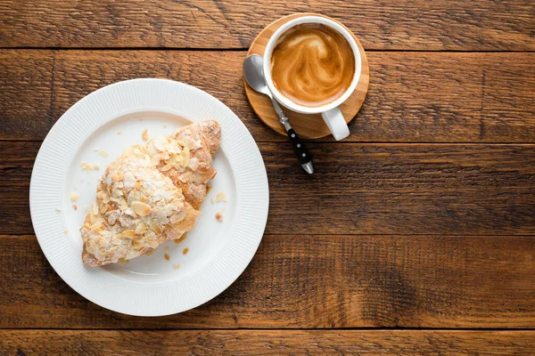 Coffee and almond croissant on a wooden table background. Top view copy space for text or design. Coffee breakfast, breakfast or lunch food