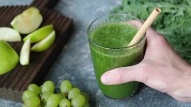 Bir bardak yeşil smoothie ile lahana, yeşil elma, kereviz, üzüm ve salatalık. Masaya bir bardak vegan detoks yeşil smoothie koyarak, bambu saman içerek
