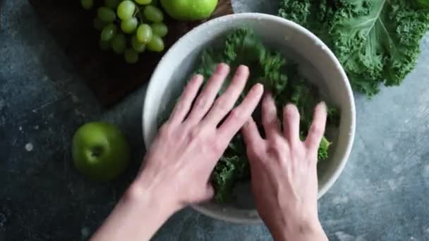 女性の手をきれいな水のボウルにケールキャベツの葉を洗う 健康的なビーガンフードを準備 デトックス食品 緑のライフスタイル トップビュー — ストック動画