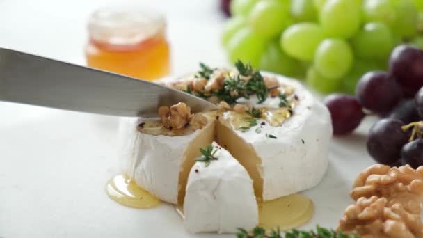 用刀切割柔软的白色奶酪Brie或Camembert 法国奶酪加蜂蜜切片 有葡萄 百里香和核桃的奶酪盘 — 图库视频影像