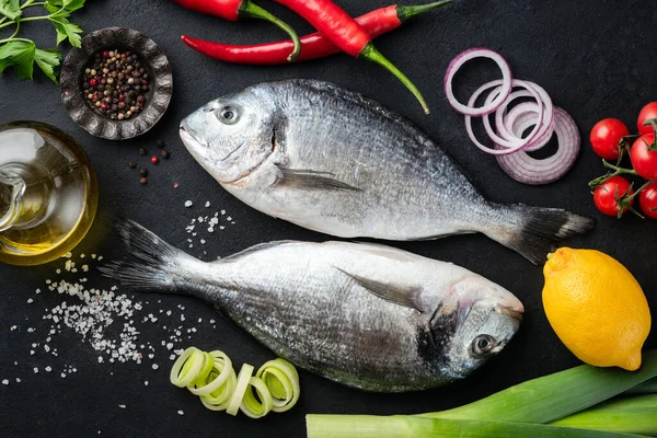 Dos pescados dorados sin cocer sobre fondo negro con especias y verduras —  Fotos de Stock