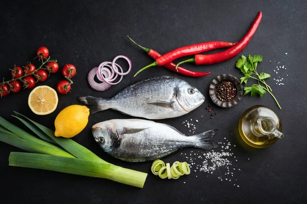 Pescado dorado sin cocer con especias y verduras sobre pizarra negra —  Fotos de Stock