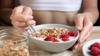 Genç fitness kadını kahvaltıda granola kasesi yiyor.