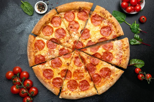 Pepperoni pizza sliced on black concrete background