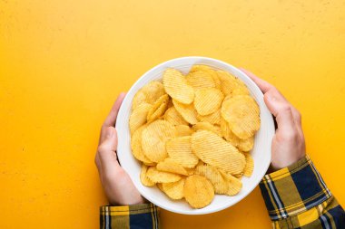 Patates cipsi ya da cips kasede erkeğin elinde sarı arka plan, üst manzara, kopyalama alanı. Superbowl atıştırmalığı, abur cubur