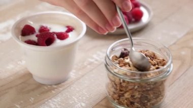 Yoğurt, granola ve böğürtlen karışımı. Yoğurt kavanozuna ahududulu granola ekliyorum. Sağlıklı kahvaltı.
