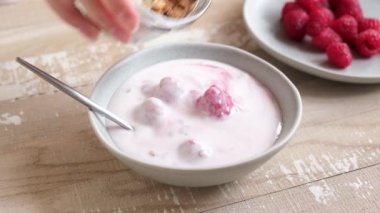 Yoğurda granola ve böğürtlen ekliyorum. Kahvaltı için kasede ahududu yoğurdu.