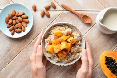 Yulaf ezmesi kasesi, üzerinde papaya olan kadın elleriyle ahşap masa arkası. Sağlıklı tropikal kahvaltı, üst manzara.