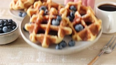 Yaban mersinli Belçika waffle 'ı, şurup ve bir fincan kahveyi ahşap masada servis etmek.