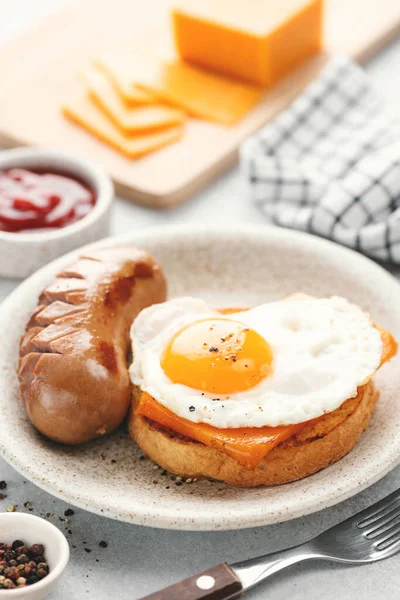 Breakfast toast with cheddar cheese, fried egg and sausage served on a plate, closeup view. English breakfast food