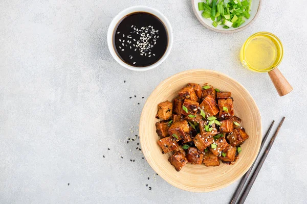 Fried marinated tofu cubes in bamboo bowl served with chopped scallions, sesame seed oil and soy sauce. Top view copy space. Asian cuisine