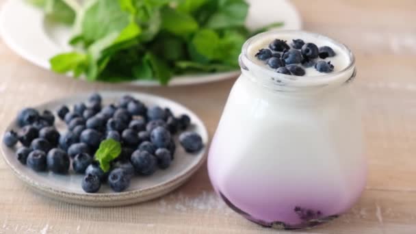 木製のテーブルの上のガラス瓶の中のブルーベリーヨーグルト ブルーベリーで天然ヨーグルトを食べる 健康食品 — ストック動画