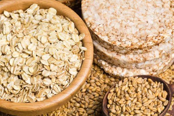 Variety of grains: rolled oats, golden linseeds (flax seeds), whole wheat grains and buckwheat cakes — Stock Photo, Image