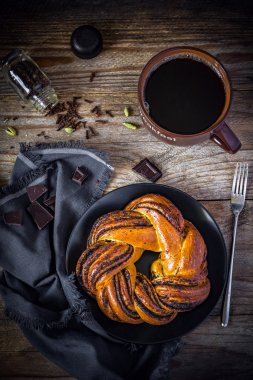 Cup of black coffee, pastry with poppy seeds and chocolate on wooden textured background. Breakfast in cafe