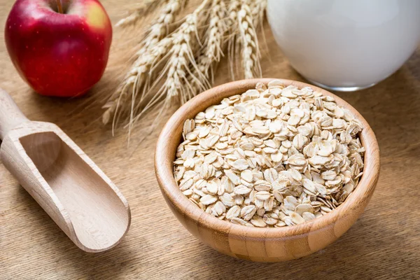 Harina de avena (copos de avena, avena enrollada), leche fresca, espigas de trigo y manzana sobre fondo de textura de madera — Foto de Stock