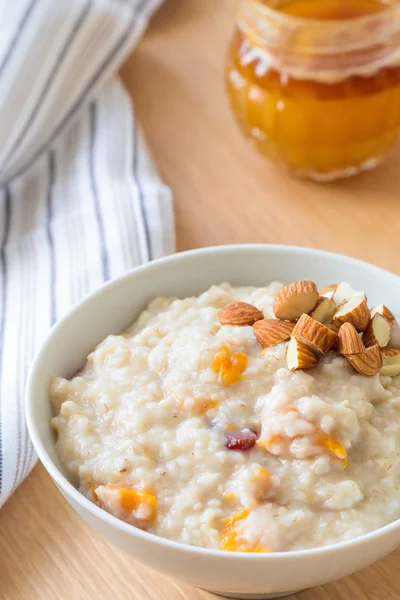 Oatmeal porridge with dried fruits, honey and nuts in bowl on breakfast table — Stock Photo, Image